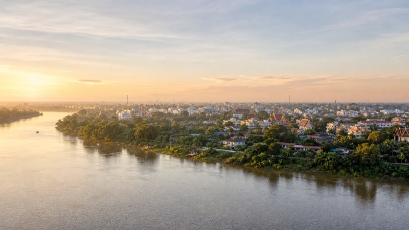 Editorial illustration of a sunset river view toward a low-rise cityscape in Ubon Ratchathani